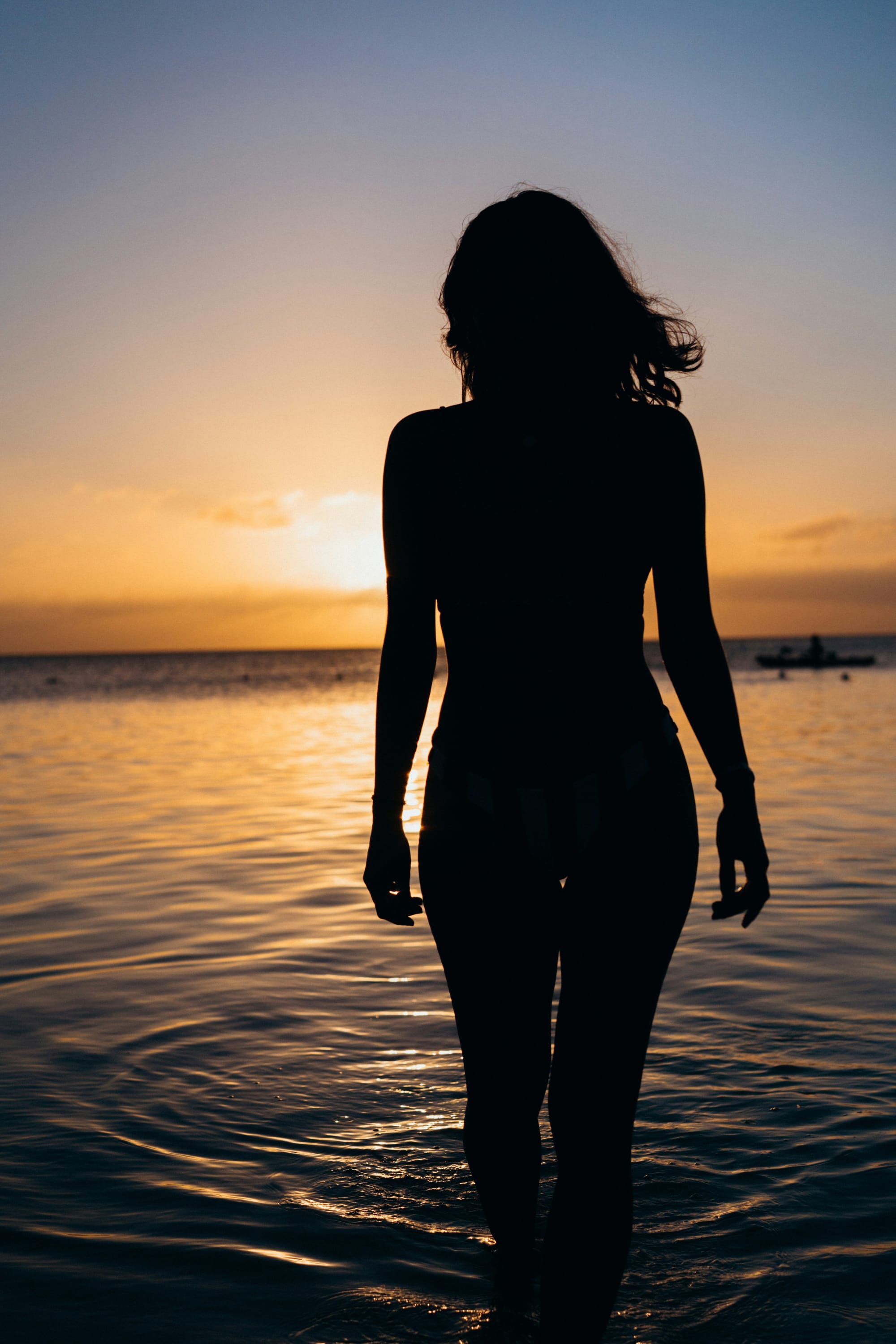 Woman in shadow, facing away and walking in water
