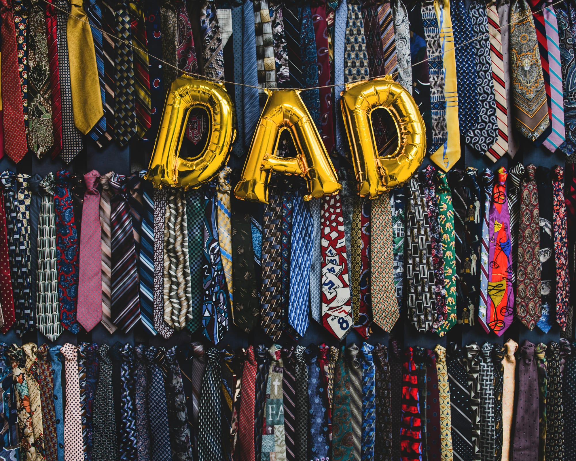 "DAD" balloons draped in front of a wall of suit ties
