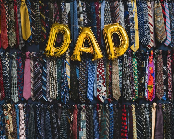 "DAD" balloons draped in front of a wall of suit ties